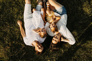 Mother, father and two daughters lying on green grass in an open field, laughing.