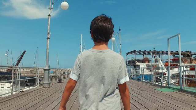 Young Boy Walking On Pier With Boats And The Ocean On Both Sides And In The Distance Gimbal Follow Shot