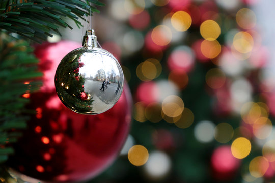 Red and silver christmas balls on a fir branches on festive golden lights background, street illumination. New Year tree with decorations, magic of a holiday for background