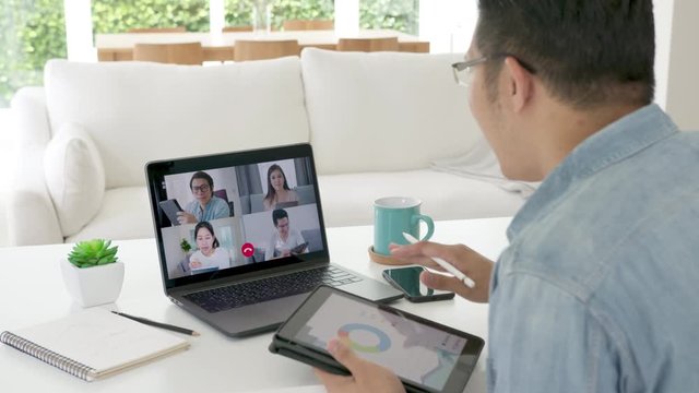 Zoom out back view : business man talking in video conference.Asian team using laptop and tablet online meeting in video call.Working from home, Working remotely and Self isolation at home
