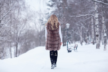 girl in a fur vest walks in the winter outside / adult young model in winter clothes fur