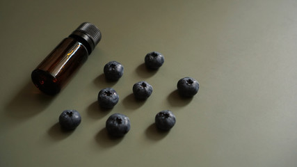 A bottle of blueberry seed essential oil and fresh blueberries on dark green background