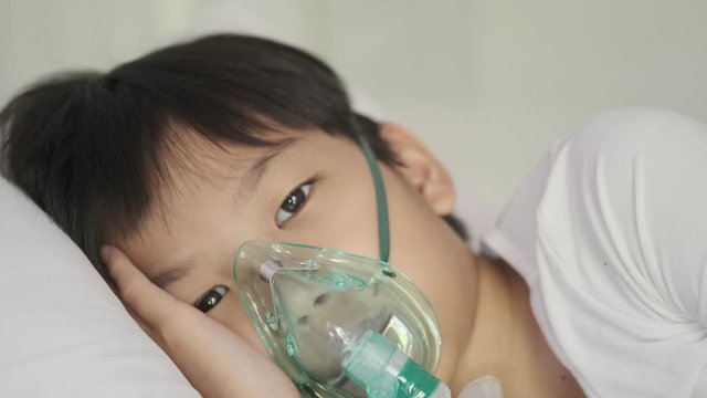 4k Young asian boy with oxygen mask sleep on a bed looking at camera with sad eye