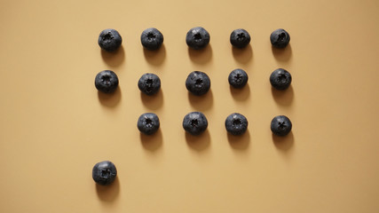 Blueberries are laid out in rows on a gold background - one berry is not in the rows, the concept...