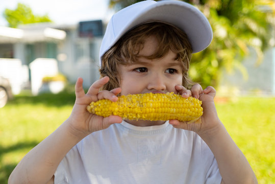 Boy Child Eating Yellow Corn With Bare Chest And Funny Face, Green Nature Background. Autumn Lifestyle. Homegrown Organic Food. Vegan Children Nutrition.