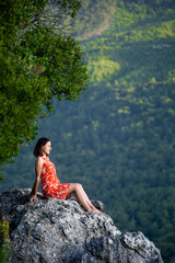 Naklejka premium A girl in a red dress sits on a large rock on top of a mountain