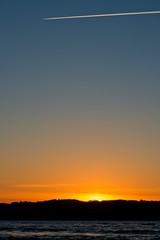 sunset on a hill with the sea in front with airplane steam trails at the top