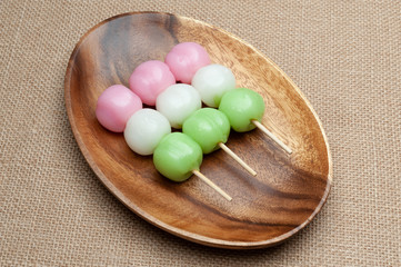 Japanese traditional sweet called Dango Mochi on wooden platter with green tea. Isolated on jute background. Close-up. Top view.