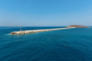 Seascape with small lighthouse on breakwater leading to islet of Palatia with Naxos Temple of Apollo Portara