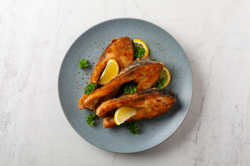 Fried carp in pieces, served on a gray plate. Marbled bright background.