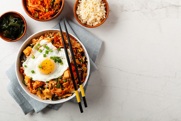 Kimchi cabbage with rice and chicken. Served in a white bowl on a light marble background.