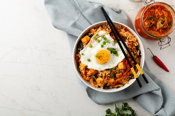 Kimchi cabbage with rice and chicken. Served in a white bowl on a light marble background.