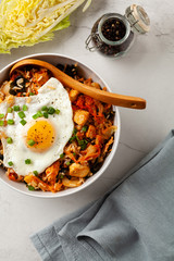 Kimchi cabbage with rice and chicken. Served in a white bowl on a light marble background.