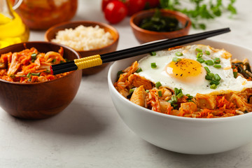 Kimchi cabbage with rice and chicken. Served in a white bowl on a light marble background.
