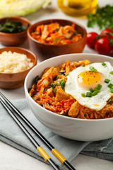 Kimchi cabbage with rice and chicken. Served in a white bowl on a light marble background.