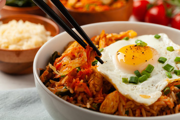 Kimchi cabbage with rice and chicken. Served in a white bowl on a light marble background.