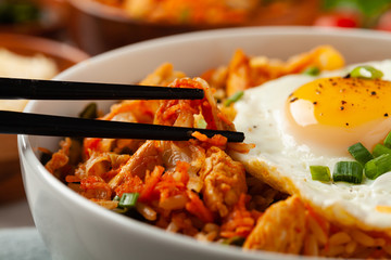 Kimchi cabbage with rice and chicken. Served in a white bowl on a light marble background.