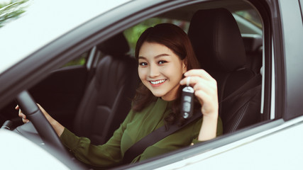 Beautiful young girl driver with car key in hand, happy owner of a new automobile