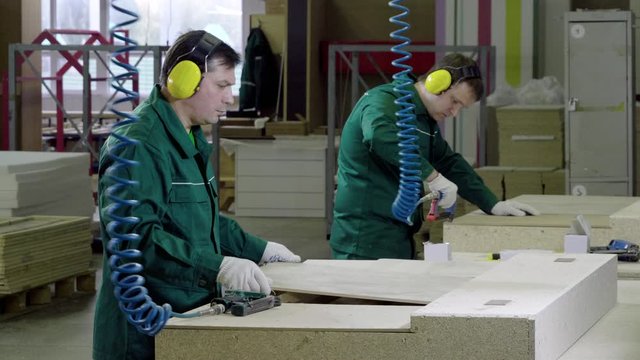 Two workers dressed in uniform make a sofa, couch or settee in a furniture factory. 4K