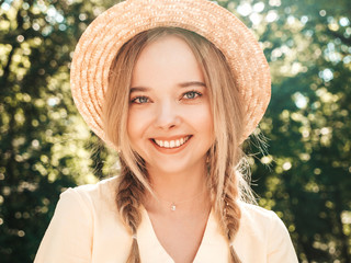 Portrait of young beautiful smiling hipster girl in trendy summer sundress. Sexy carefree woman posing on the street background in the park in hat at sunset. Positive model outdoors