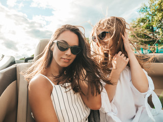 Portrait of two young beautiful and smiling hipster girls in convertible car. Sexy carefree women...