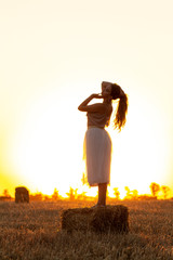 Fototapeta na wymiar silhouette woman figure at sunset standing on hay stack, beautiful romantic girl with long hair posing outdoors in field