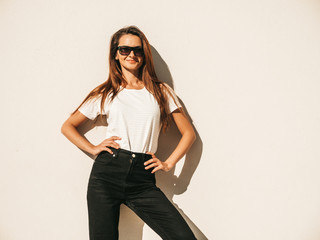 Portrait of beautiful model in sunglasses. Female dressed in summer hipster white T-shirt and jeans. Trendy girl posing near wall in the street. Funny and positive woman having fun outdoors