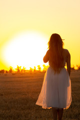 Fototapeta na wymiar graceful silhouette figure of young woman walking in field at sunset, beautiful romantic girl with long hair outdoors