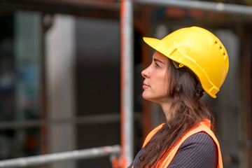 Profile portrait of an attractive female factory worker wearing a yellow protective helmet and looking aside