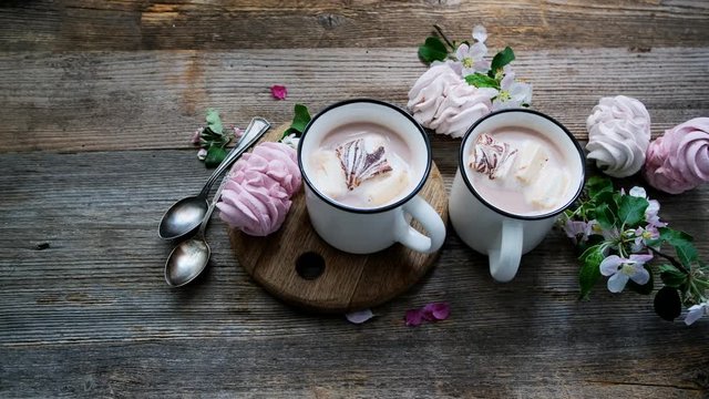 Tasty marshmallow and cups with cocoa near spring flowers