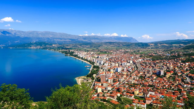 City buildings with red roofs at the shore of a lake with mountains in the background. View of Pogradec city and Ohrid lake, Pogradec, Albania