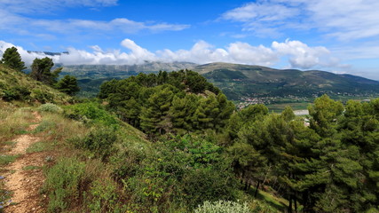 Walking path in lovely green nature with clouds and mountains in the background during a sunny day, Berat