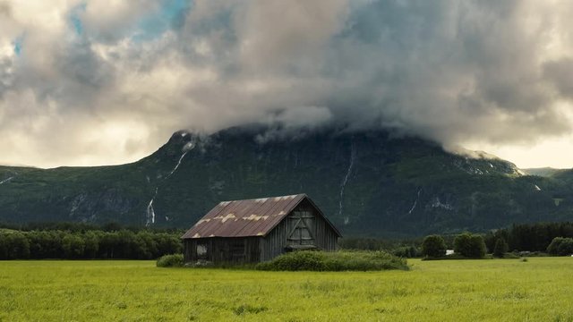 Wooden  Barn House Surrounded By Lush Green Grass With Mountain At The Background - Wide Shot