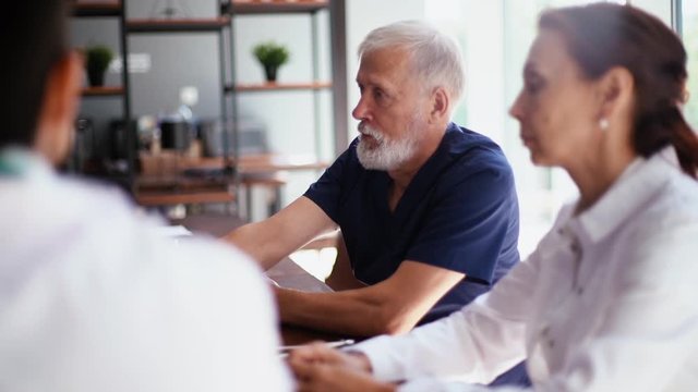 Medical team of professional doctors on meeting in medical office discussion about new treatment for patient sitting at the desk in modern conference office room. Tracking shot in slow motion.