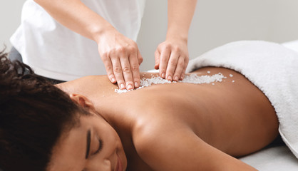 Obraz na płótnie Canvas African american lady getting salt massage at modern spa