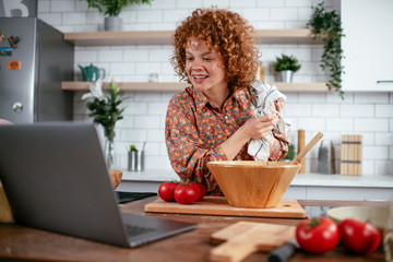 Beautiful woman in kitchen. Young woman cooking while having video call.