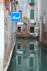 
narrow internal canal in Venice with signs indicating the passage reserved for rowing boats