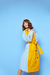  beautiful woman in a coat with striped sleeves leaned back and looks to the side against a blue background