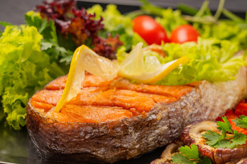 Serve food in the restaurant. Food poster - large portion of red fish, trout, salmon steak with grilled vegetables, salad, broccoli and tomatoes, decorate with lemon and rosemary.