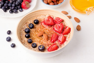 Healthy breakfast of oatmeal with strawberries, blueberries and almonds, sprinkled with honey