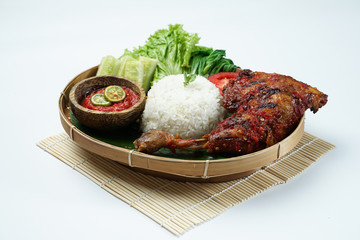 Spicy grilled chicken with ripe red skin laid out on a wooden sheet on a white background, plus white rice, chili sauce and various vegetables, view from above. commonly used for menus and box wrap im