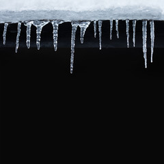 Small icicles spike of ice hanging from the roof. Winter subfreezing weather or spring snowbreak concept. Black background copy space.