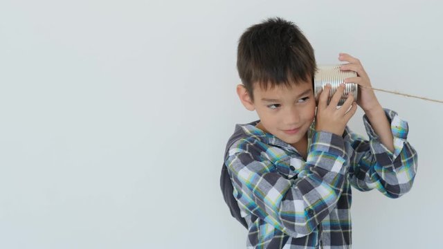 Little boy listening message from wire handmade telephone on wall background