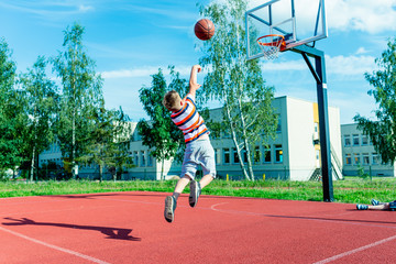 Attractive east european caucasian little basketball player jumps to throw the ball into the hoop.outdoors red court