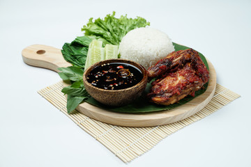 Spicy grilled chicken with ripe red skin laid out on a wooden sheet on a white background, plus white rice, chili sauce and various vegetables, view from above. commonly used for menus and box wrap im