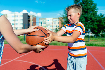 Attractive caucasian two little basketball players holds ball on a outdoors red court