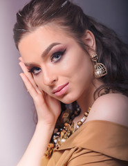 Profile of Young Caucasian Woman with Golden Jewelry. She Wears a Statement Necklace With Flowers and Stones and a Pair of Earrings with Big Pearls, on Grey Background