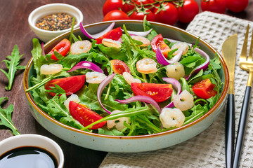 Mediterranean diet menu concept Healthy salad of fresh vegetables - tomatoes, arugula, purple onions in plate, sesame seed, soy sauce, knife, fork, napkin on wooden table Vegan food Flat lay Top view