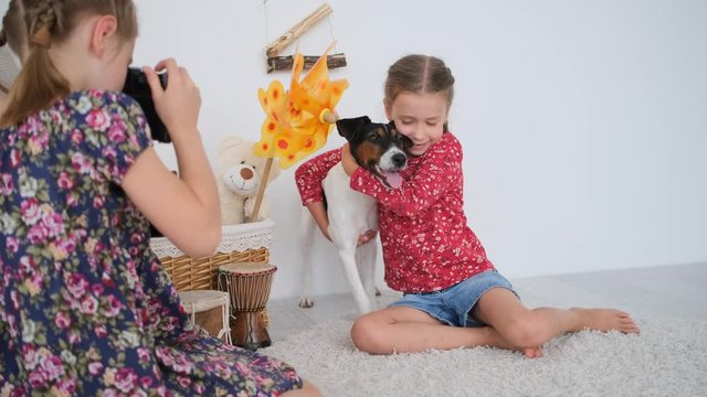Little girl taking pictures with film camera of sister with fox terrier dog sitting on floor in light room