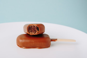 Chocolate cake in the form of ice cream on a stick on a white plate and a colored background
